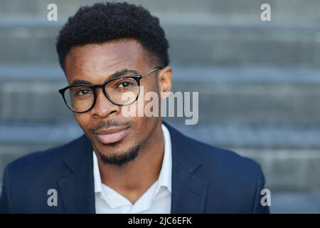 Portrait of content handsome young smart African-American man in eyeglasses sitting on staircase outdoors Stock Photo