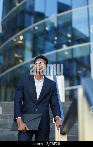Serious ambitious young Afro-American businessman in glasses moving down staircase and contemplating cityscape Stock Photo