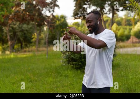 Happy young adult african american man enjoying music and dancing in the park wearing headphones Stock Photo