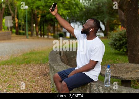 Young adult man resting in the park after jogging and taking a selfie. Healthy lifestyle. Stock Photo