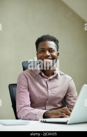 Portrait of positive young bearded African-America IT engineer sitting in front of laptop in modern office Stock Photo