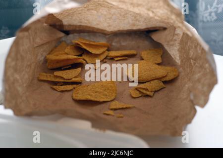 Brown paper bag with few Mexican nachos or chips in it. Most of the food is already eaten. Takeaway fast food - unhealthy yet easy and delicious food. Stock Photo
