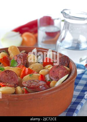 a traditional greek plate with pork sausage,beans, red pepper and tomato sauce.It is served in a ceramic bowl with a glass of ouzo . Stock Photo