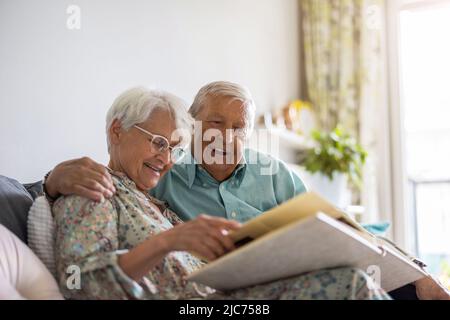 Elderly couple looking at a photo album while sitting on a sofa Stock Photo