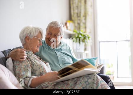 Elderly couple looking at a photo album while sitting on a sofa Stock Photo