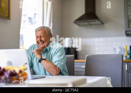 Elderly man using laptop at kitchen table Stock Photo