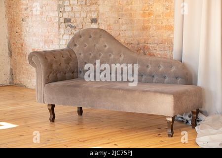 gray upholstered armchair carried a brick brown wall in an apartment on a wooden floor, upholstered furniture at home, design and interior Stock Photo