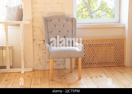 soft gray armchair in the hall near the window, upholstered furniture in the apartment, armchair in the hall, minimalism Stock Photo