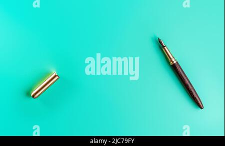 Wooden and gold fountain ink pen, opened, cap on the left, blue green background top down view, space for text middle Stock Photo