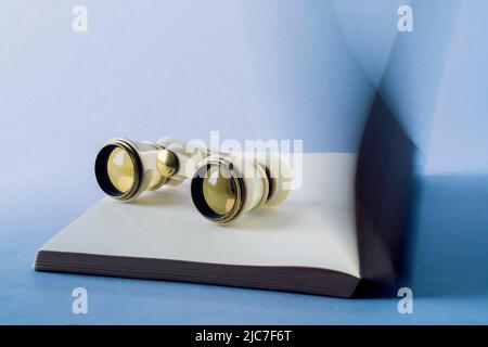 Binoculars on a open book. Turning pages. Reading books exploring new adventures and looking other life experience Stock Photo