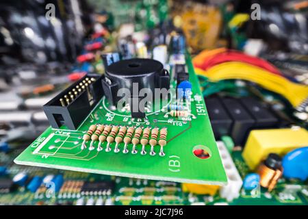 Various electronic components at green PCB in e-waste heap detail. Closeup of black piezoelectric buzzer, connector or resistors..Old PC part disposal. Stock Photo