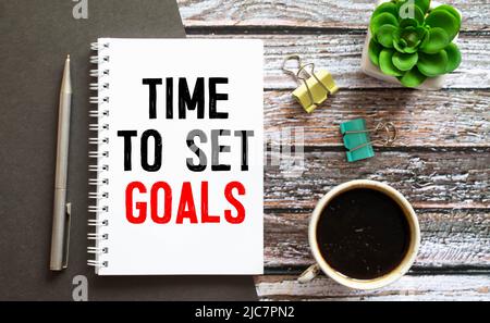 TIME TO SET GOALS is written in a white notepad near a white alarm clock on a black background. Stock Photo