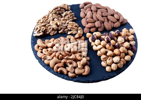 Various nuts sorted on black stone plate isolated on white background. Round stone plate. Asoorted nuts close up Stock Photo