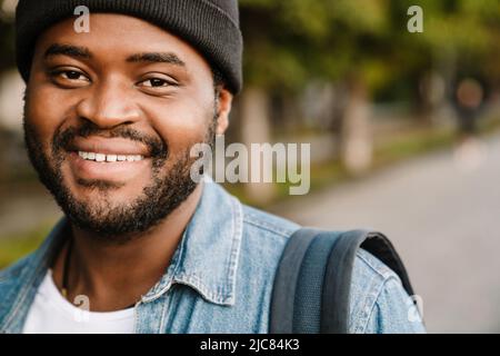 Black young man wearing hat smiling while walking in summer park Stock Photo