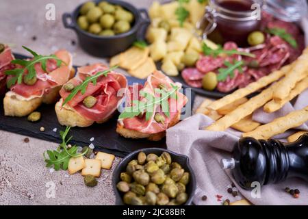 bruschetta with prosciutto ham and capers with traditional antipasto meat plate on background Stock Photo