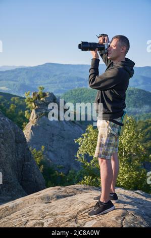 Nature photographer with digital camera on top of the mountain in the morning, taking photo of sunset mountains. Concept of travel lifestyle. Stock Photo