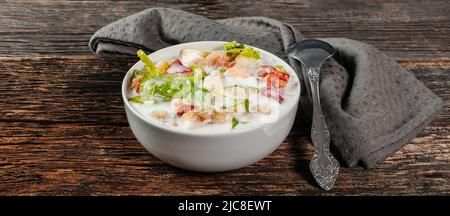 Traditional Russian cold soup okroshka with fresh potato, cucumber, tomato, boiled eggs and kefir. Flat lay, wooden background Stock Photo