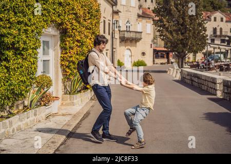 Dad and son tourists enjoying Colorful street in Old town of Perast on a sunny day, Montenegro. Travel to Montenegro concept. Scenic panorama view of Stock Photo