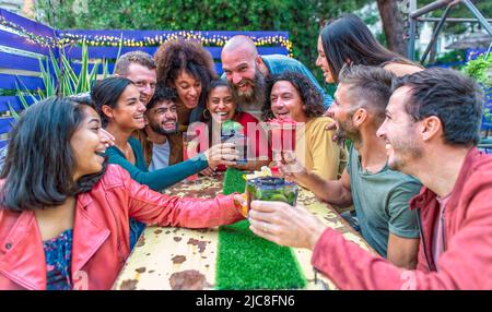 multiethnic group of friends sitting on a table in a lounge bar restaurant making toast with wonderful gourmet cocktail. diverse people celerating Stock Photo