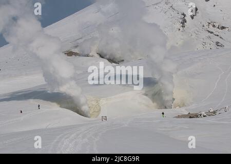 Mountain climbers standing next to volcanic vents emitting smoke Stock Photo
