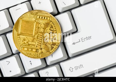 Gold bitcoin coin, reverse side lying on white computer keyboard. Stock Photo