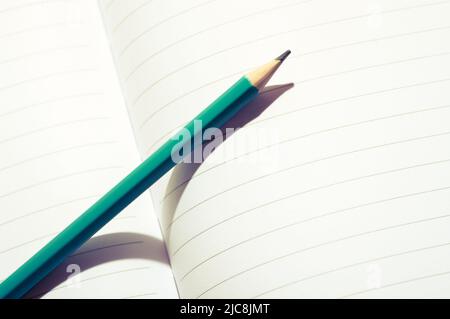 Aqua blue pencil on an open notebook. Close up image of a pencil on white paper. Stock Photo
