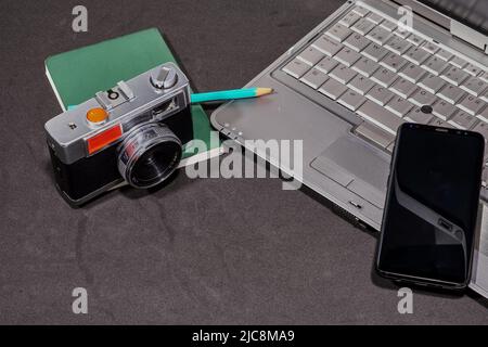 Top view of a photo camera, a laptop, a blank notepad with a green pencil and a cell phone, on a gray table. Copy space. Stock Photo
