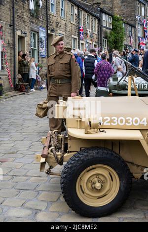 Haworth 1940's weekend (man dressed in khaki WW 2 costume as soldier looking at Jeep on busy steep crowded Main Street) - West Yorkshire, England UK. Stock Photo