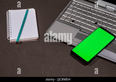Composition, laptop, notebook and a mobile with a green screen. Stock Photo