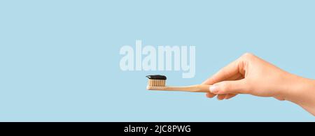 Female hand holding bamboo brush with activated charcoal toothpaste on light blue background with space for text Stock Photo