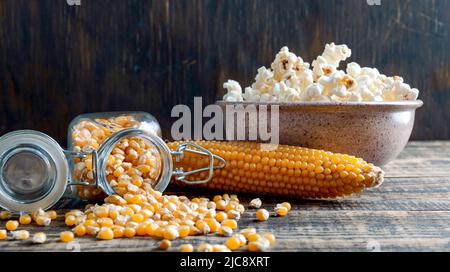 Uncooked corn kernels spilled out of a jar on a wooden table. The concept of making popcorn at home. Stock Photo