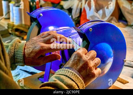 Hands of an elderly man sharpening a knife on a blue grinder Stock Photo