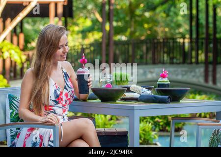 Young woman in modern trendy outdoor cafe, drinking healthy vegan juice