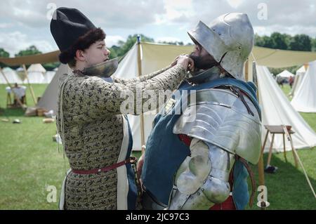 London, UK. 11th June 2022. Barnet Medieval Festival. A solider from Beaufort Companye re-enactment group is assisted from his amour after battle. Historical reenactors commemorate the Battle of Barnet in north London. A key encounter fought during the War of the Roses on 14th April 1471, the military action helped secure the throne for Edward VI. Credit: Guy Corbishley/Alamy Live News Stock Photo