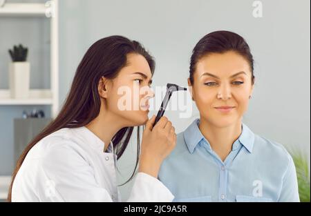 ENT doctor uses otoscope to examine young woman's ear during medical checkup in office Stock Photo