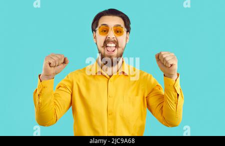 Happy stylish funny funky crazy hipster guy shouting with joy on light blue background. Stock Photo