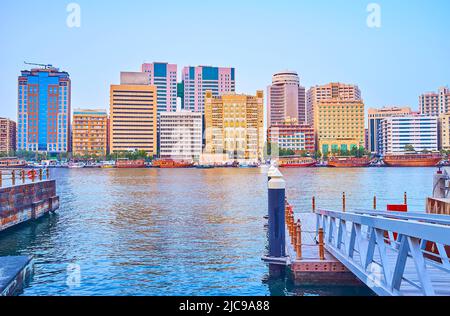 The embankment of Deira neighborhood with lines of modern buildings and vintage wooden dhow boats behind Dubai Creek, UAE Stock Photo