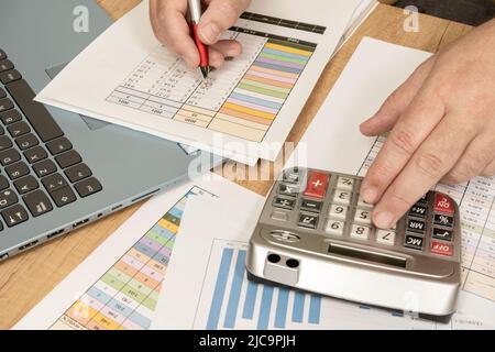 Sitting white man doing accounts with a calculator and reviewing cash and money flows, projections and invoices. Concept work at home, checking accoun Stock Photo