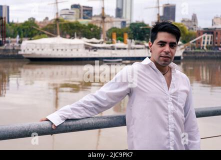 Elegant young Latino man leaning on a railing with the old port in the background.. Stock Photo