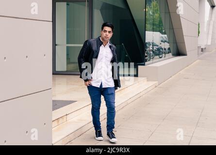 Young latino guy coming out of a building while observing or looking at the street. Modern clothing. Stock Photo