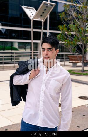 Young man holding his jacket with his hand on his shoulder with a building in the background Stock Photo