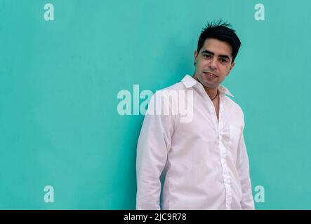 Half-length photograph of a young Latino guy leaning against a plain colored wall. Urban clothing. Stock Photo
