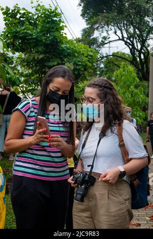 Medellin, Antioquia, Colombia - February 19 2022: A Brunette Woman Shows a Photo on her Phone to a Blonde Woman with Glasses Wearing a Camera around h Stock Photo