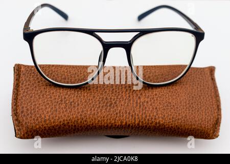 Black frame spectacles made of acetate material kept on a brown leather case on white background Stock Photo