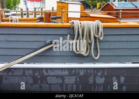 Close-up of ropes looped over the side of a vintage wooden sailing ship on a wet day with glimpses of hold harbor behind Stock Photo