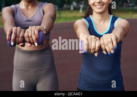 Close up diverse women holding dumbbells and doing exercises outdoors Stock Photo