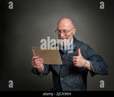smiling and positive senior man is chatting online using a digital tablet, thumbs up hand gesture Stock Photo