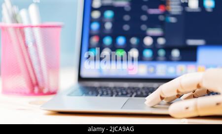 Robotic arm using laptop on a wooden table. Artificial intelligence robot working on an open laptop. Futuristic robot hand typing and working with lap Stock Photo