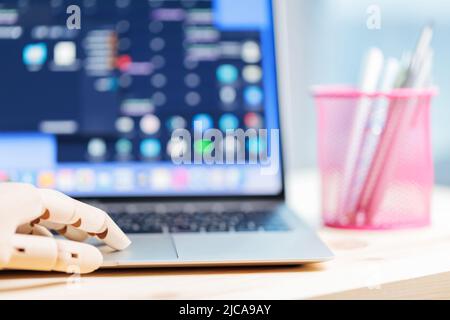 Robotic arm using laptop on a wooden table. Artificial intelligence robot working on an open laptop. Futuristic robot hand typing and working with lap Stock Photo
