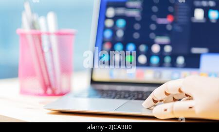 Robotic arm using laptop on a wooden table. Artificial intelligence robot working on an open laptop. Futuristic robot hand typing and working with lap Stock Photo